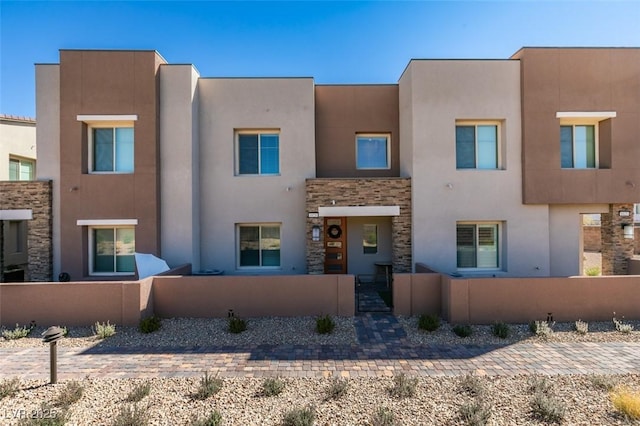 view of front of house featuring stone siding, a fenced front yard, and stucco siding