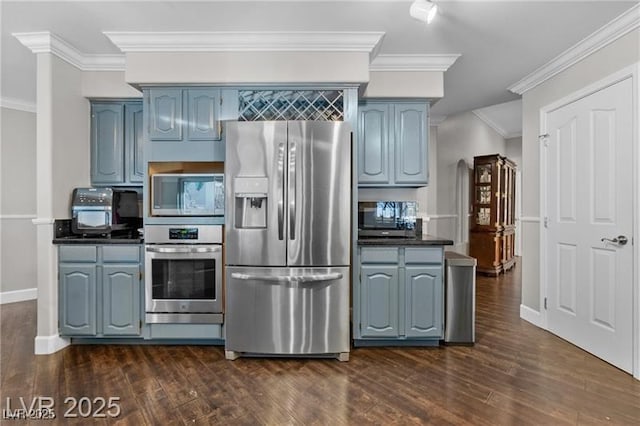 kitchen with blue cabinetry, dark countertops, appliances with stainless steel finishes, dark wood-type flooring, and ornamental molding