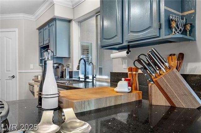 kitchen featuring blue cabinets, dark stone counters, ornamental molding, and a sink