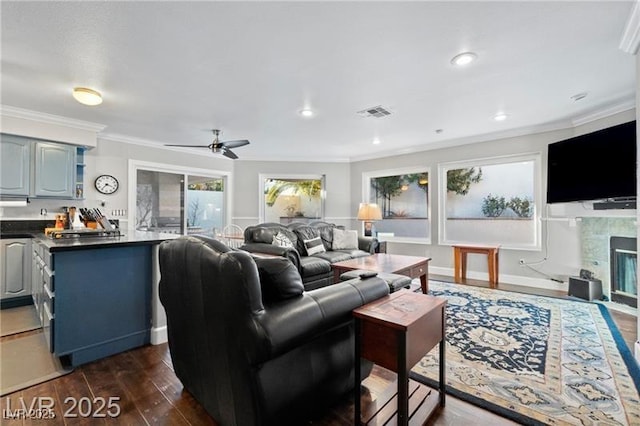 living room featuring visible vents, ceiling fan, a fireplace with flush hearth, dark wood-style flooring, and crown molding