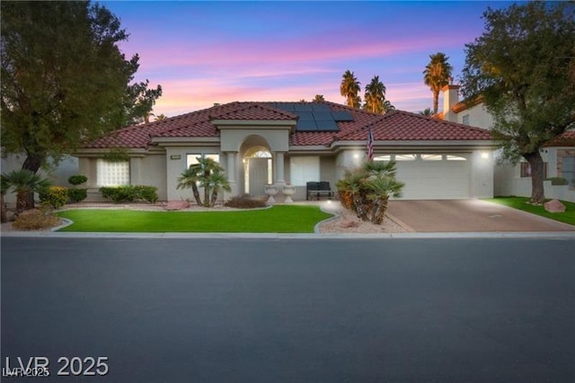 mediterranean / spanish-style home with an attached garage, a tile roof, roof mounted solar panels, and stucco siding