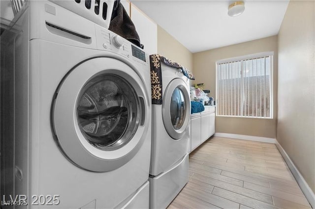 washroom featuring light wood-type flooring, cabinet space, baseboards, and separate washer and dryer