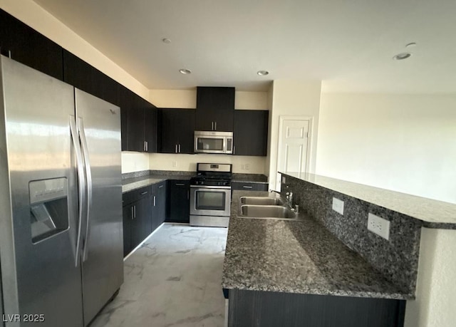 kitchen with marble finish floor, stainless steel appliances, a kitchen island with sink, a sink, and dark cabinets