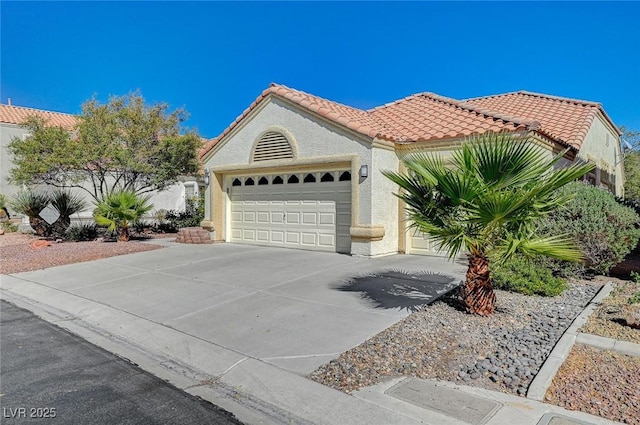 mediterranean / spanish house with driveway, an attached garage, a tile roof, and stucco siding