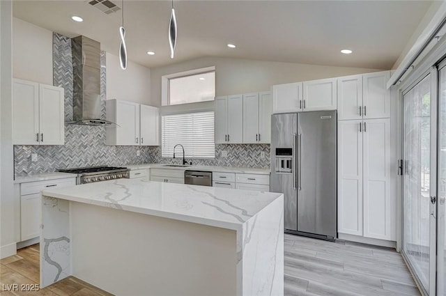 kitchen featuring lofted ceiling, visible vents, appliances with stainless steel finishes, a kitchen island, and wall chimney range hood