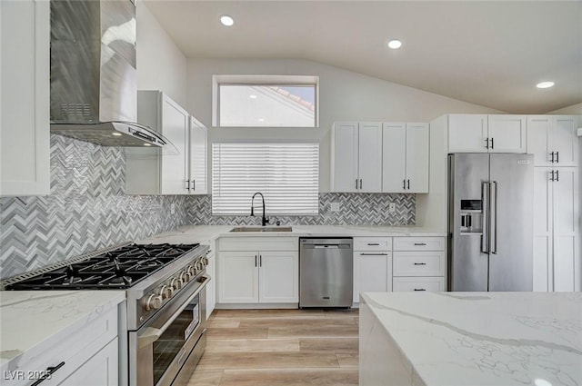 kitchen featuring wall chimney exhaust hood, high quality appliances, light stone countertops, vaulted ceiling, and a sink