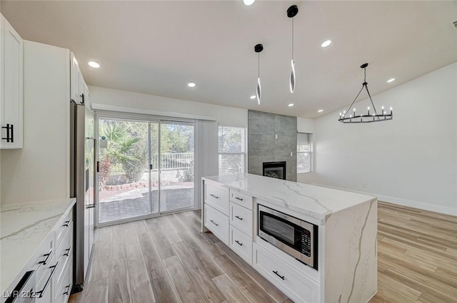 kitchen featuring open floor plan, light wood-style flooring, stainless steel microwave, and refrigerator with ice dispenser