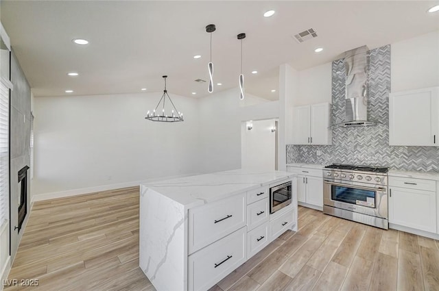 kitchen with light wood finished floors, appliances with stainless steel finishes, wall chimney range hood, and visible vents