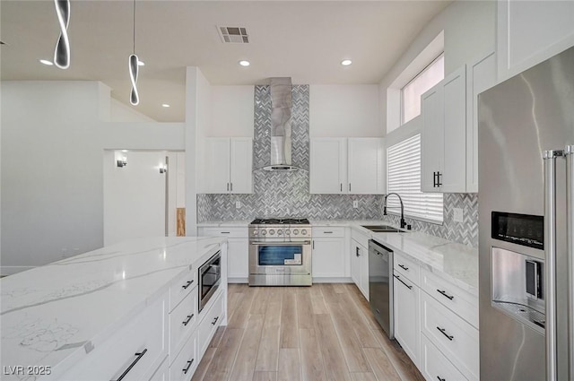 kitchen featuring light wood finished floors, visible vents, appliances with stainless steel finishes, a sink, and wall chimney range hood