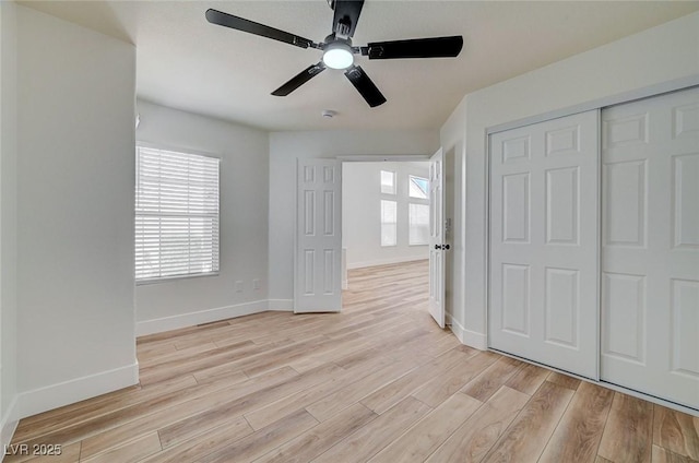 unfurnished bedroom featuring baseboards, ceiling fan, a closet, and light wood-style floors