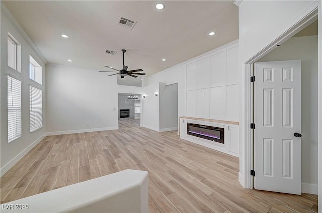 unfurnished living room with ceiling fan, light wood finished floors, a glass covered fireplace, and crown molding