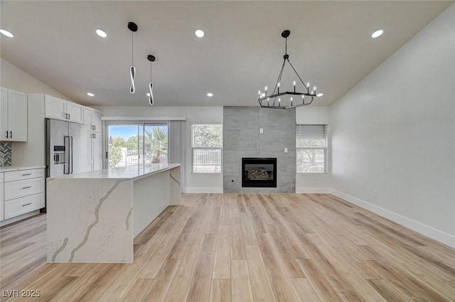 kitchen featuring light wood-type flooring, a healthy amount of sunlight, high quality fridge, and lofted ceiling