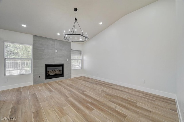 unfurnished living room featuring light wood-type flooring, a tile fireplace, a wealth of natural light, and baseboards