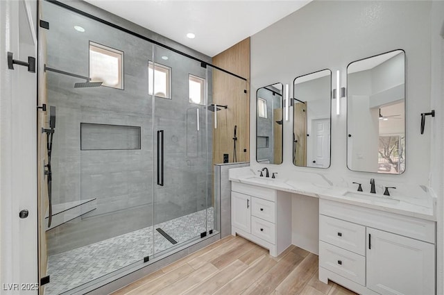 bathroom with double vanity, a sink, a shower stall, and wood finished floors