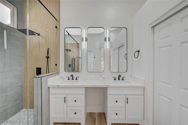 bathroom featuring a stall shower, wood finished floors, a sink, and double vanity