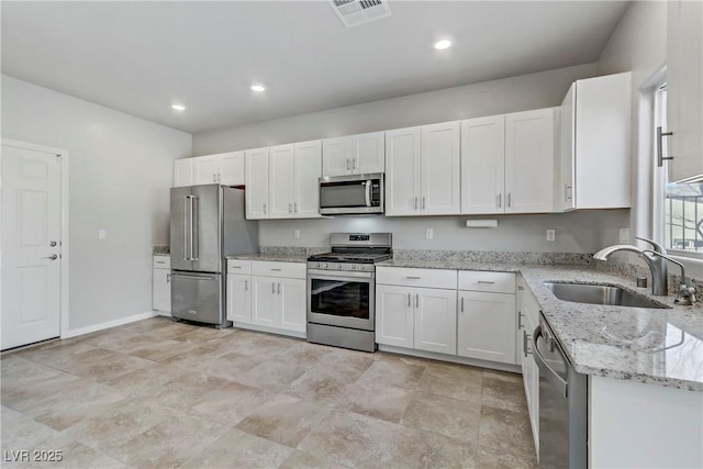 kitchen with visible vents, white cabinets, light stone countertops, stainless steel appliances, and a sink