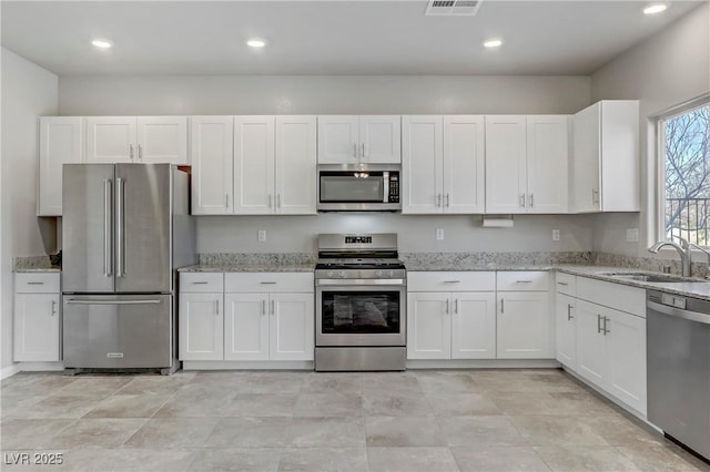 kitchen with stainless steel appliances, a sink, light stone countertops, and white cabinets