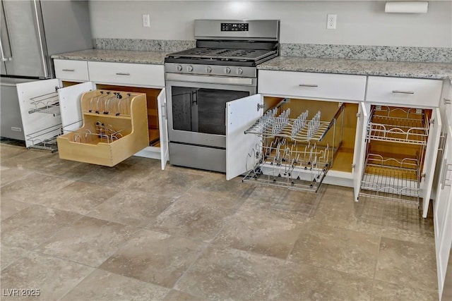 kitchen with light stone counters, gas stove, and white cabinetry