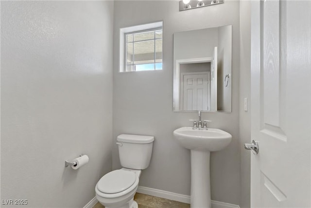 half bath with baseboards, a sink, and toilet