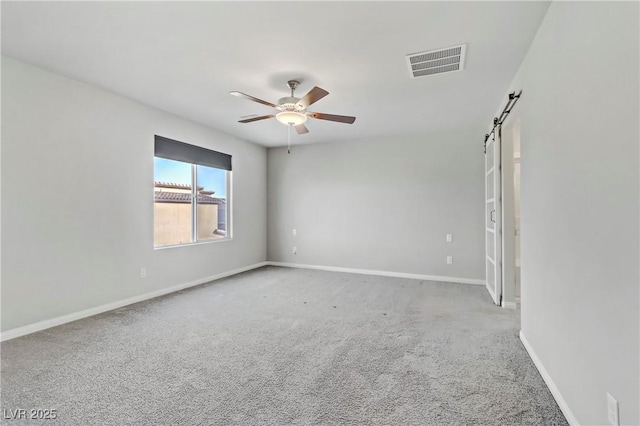 empty room with carpet, visible vents, a barn door, ceiling fan, and baseboards