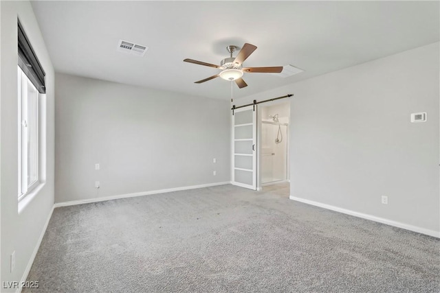 carpeted spare room featuring ceiling fan, a barn door, visible vents, and baseboards