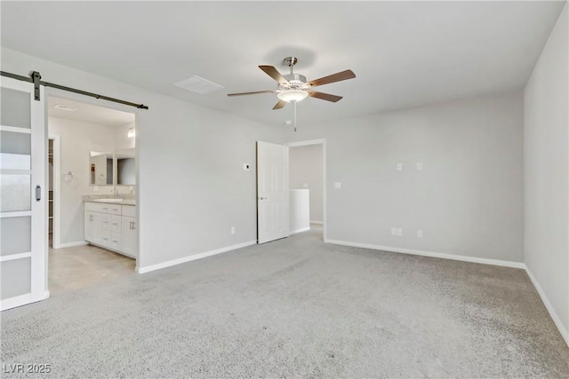 unfurnished bedroom with ceiling fan, a barn door, connected bathroom, and baseboards