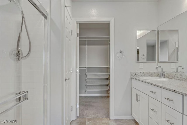 full bath featuring baseboards, a walk in closet, tiled shower, and vanity