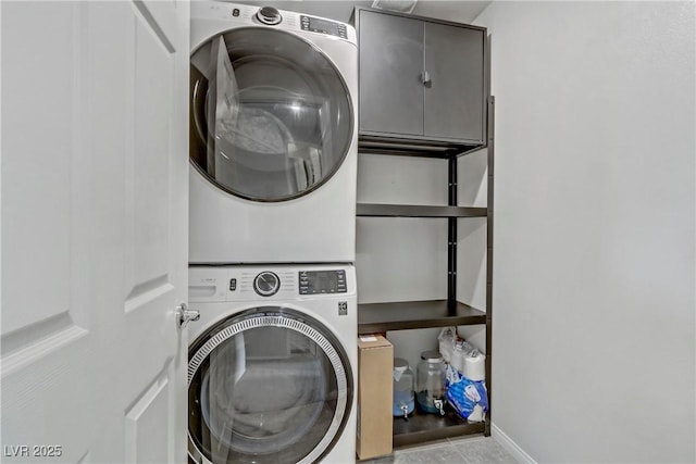 laundry area featuring baseboards, cabinet space, and stacked washer / drying machine