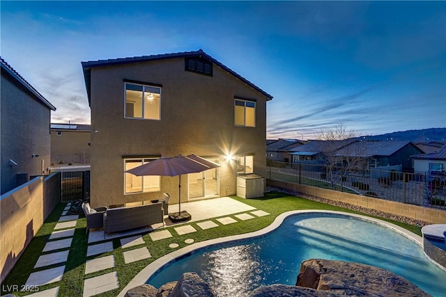 back of property at dusk with a fenced in pool, a fenced backyard, a patio area, outdoor lounge area, and stucco siding