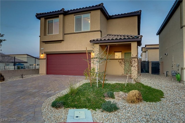 mediterranean / spanish-style house with an attached garage, fence, decorative driveway, and stucco siding