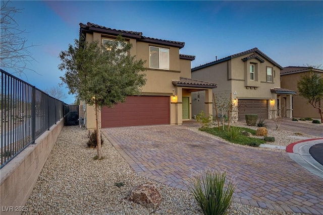 mediterranean / spanish-style home featuring a tiled roof, an attached garage, fence, decorative driveway, and stucco siding