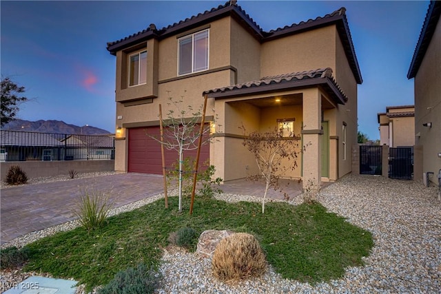 mediterranean / spanish-style house with a garage, decorative driveway, fence, and stucco siding