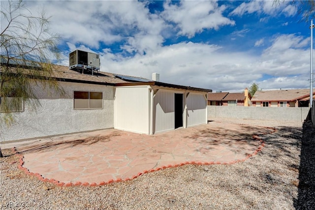 rear view of house featuring fence, central air condition unit, roof mounted solar panels, stucco siding, and a patio area