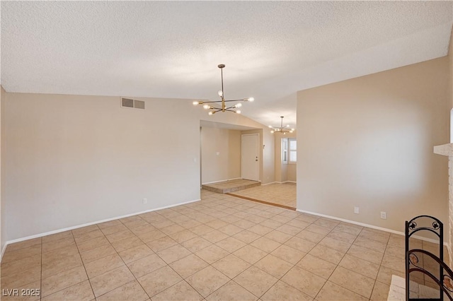 spare room featuring visible vents, vaulted ceiling, a fireplace, a notable chandelier, and a textured ceiling