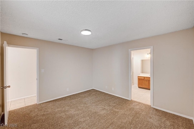 spare room featuring light carpet, visible vents, a textured ceiling, and baseboards