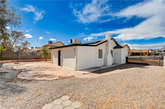 rear view of property with stucco siding, a gate, a fenced backyard, solar panels, and a patio area