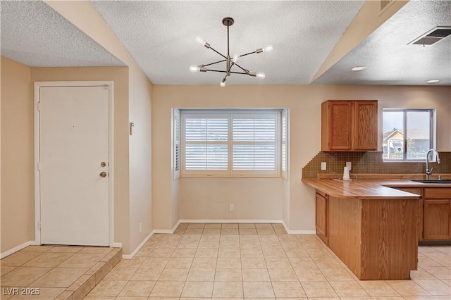 kitchen featuring tasteful backsplash, visible vents, brown cabinetry, light tile patterned flooring, and a sink