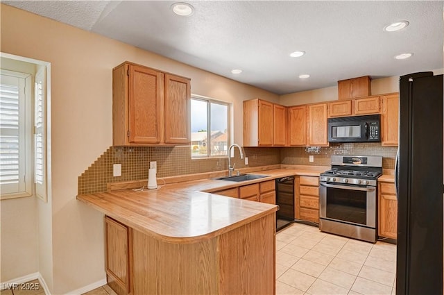 kitchen featuring black appliances, a sink, tasteful backsplash, a peninsula, and light countertops