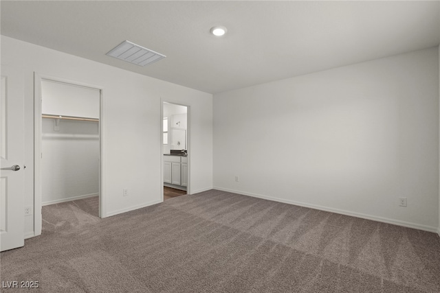 unfurnished bedroom featuring baseboards, visible vents, a walk in closet, carpet flooring, and a closet