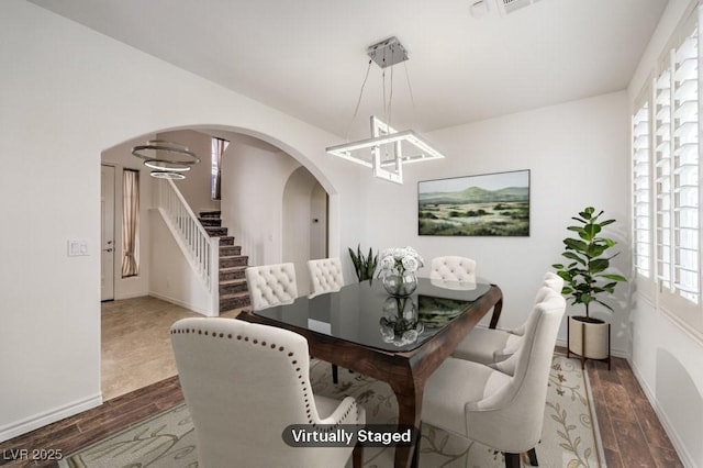 dining space featuring baseboards, stairs, arched walkways, and wood finished floors