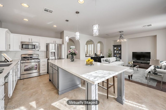 kitchen featuring visible vents, arched walkways, appliances with stainless steel finishes, white cabinetry, and backsplash