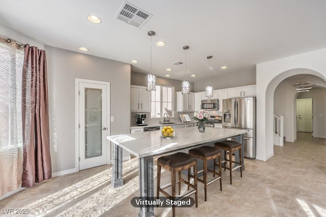 kitchen with a breakfast bar area, stainless steel appliances, visible vents, a sink, and a kitchen island