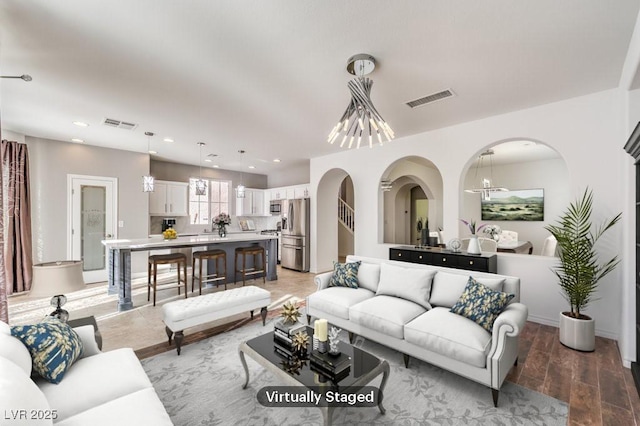 living area featuring arched walkways, recessed lighting, visible vents, and light wood-style floors