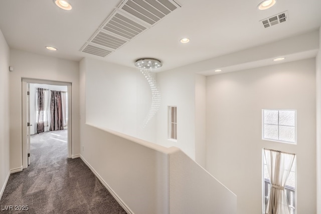 corridor featuring dark colored carpet, a healthy amount of sunlight, and visible vents