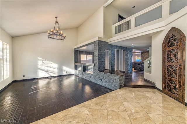 foyer entrance with baseboards, a glass covered fireplace, wood finished floors, high vaulted ceiling, and a notable chandelier