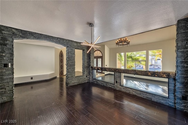 interior space featuring a notable chandelier, wood tiled floor, arched walkways, and a textured ceiling