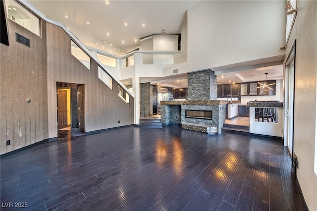 unfurnished living room with a stone fireplace, a high ceiling, and wood finished floors