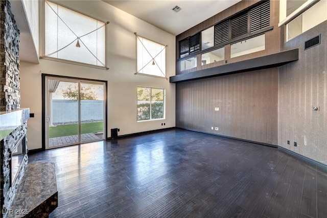 unfurnished living room with a stone fireplace, a high ceiling, wood finished floors, and visible vents