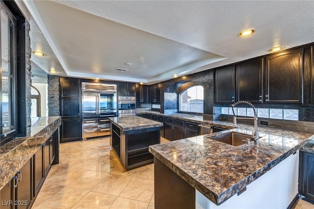 kitchen with a textured ceiling, a peninsula, a sink, visible vents, and a tray ceiling