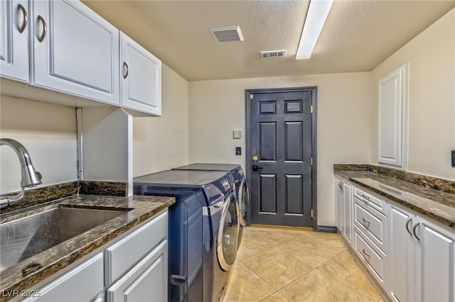 clothes washing area featuring washing machine and dryer, cabinet space, a sink, and visible vents